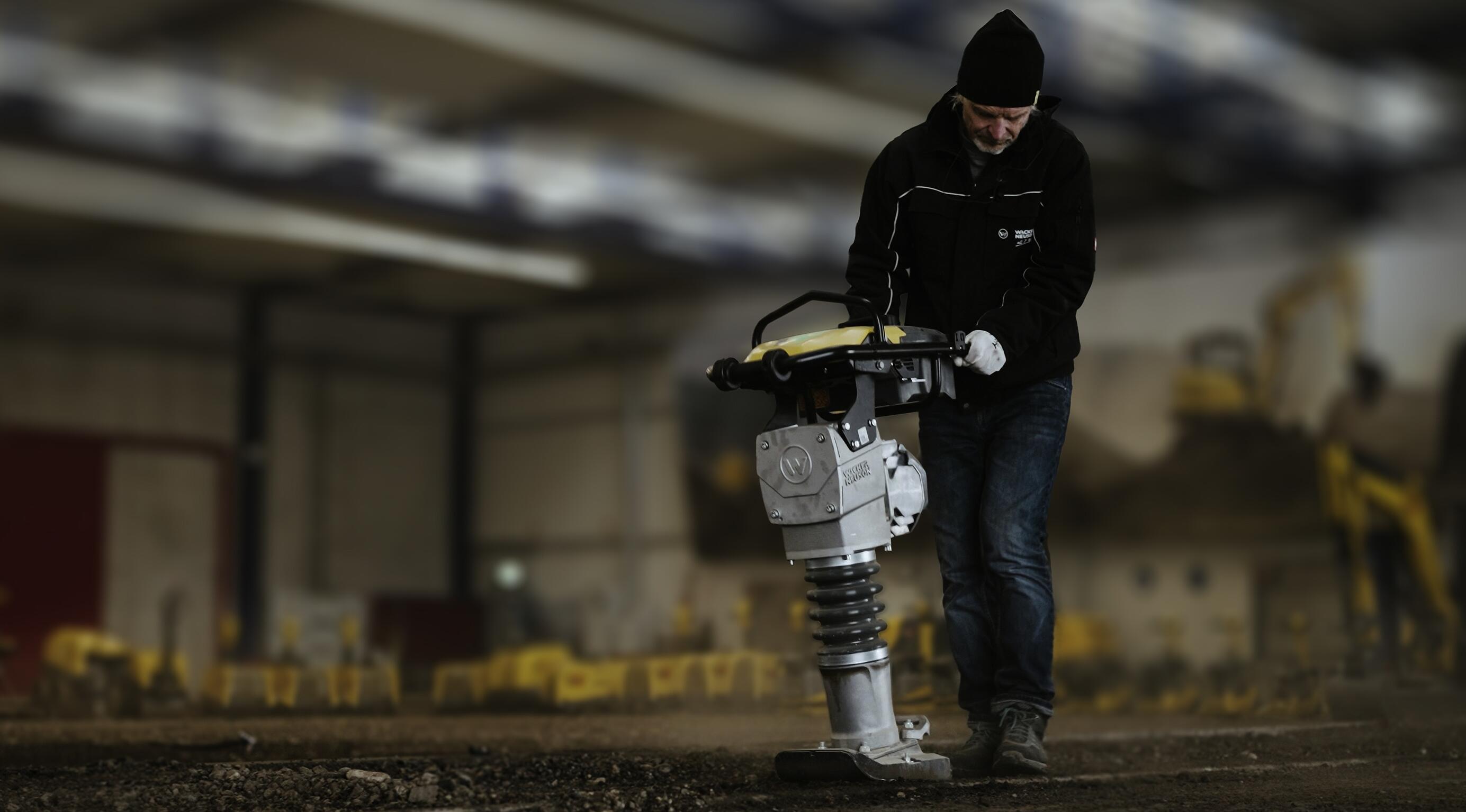 Arbeider som betjener en stampemaskin for jordkomprimering i et innendørs opplæringsmiljø for bygg- og anleggsarbeid