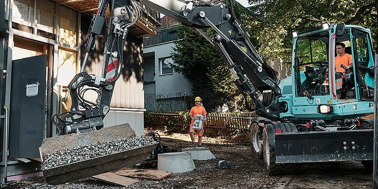Wacker Neuson EW100 hjulgravemaskine, der håndterer bulkmateriale med en vippeskuffe på en byggeplads.