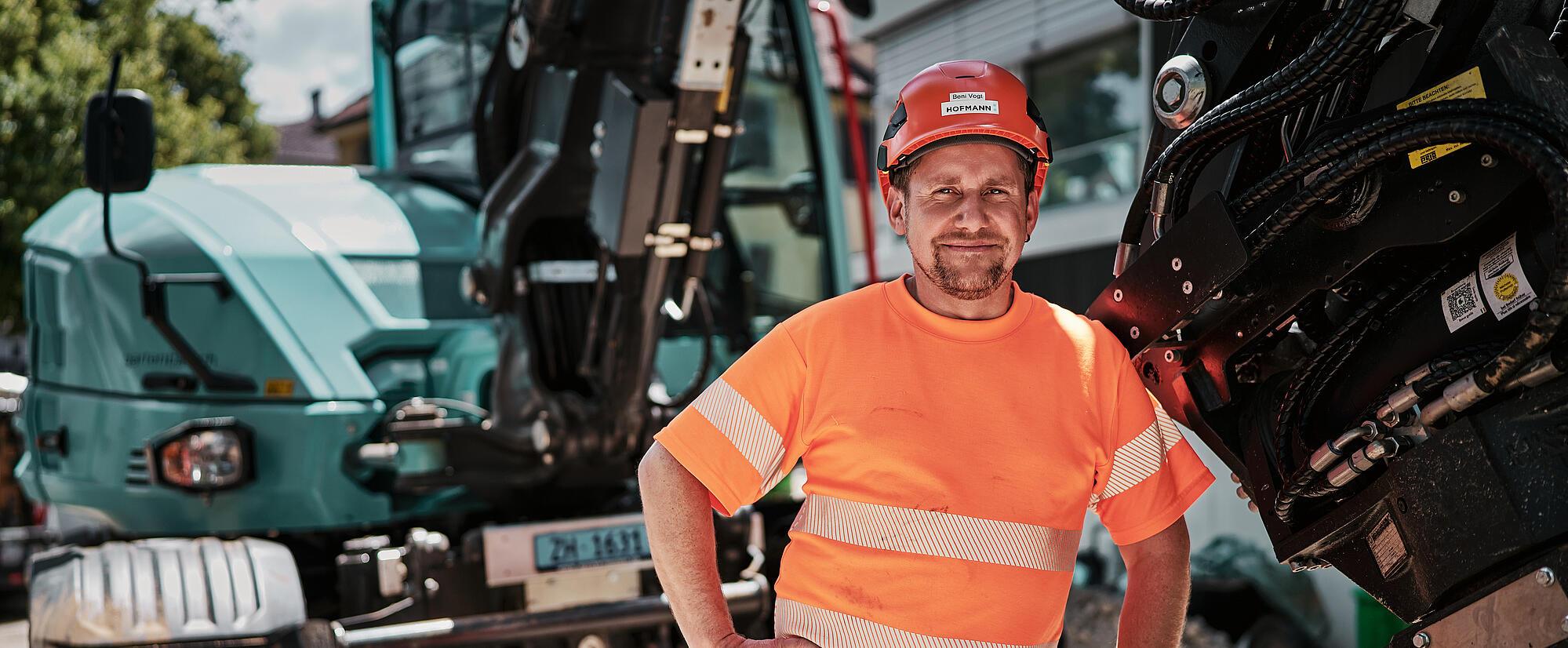 En anleggsarbeider står ved siden av en Wacker Neuson EW100 hjulgravemaskin utstyrt med et hydraulisk redskap.