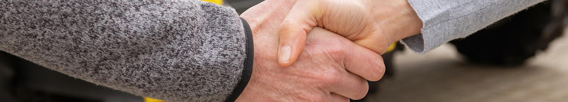 Apretón de manos entre una empleada de Wacker Neuson y un cliente, con las máquinas para la construcción de Wacker Neuson de fondo.