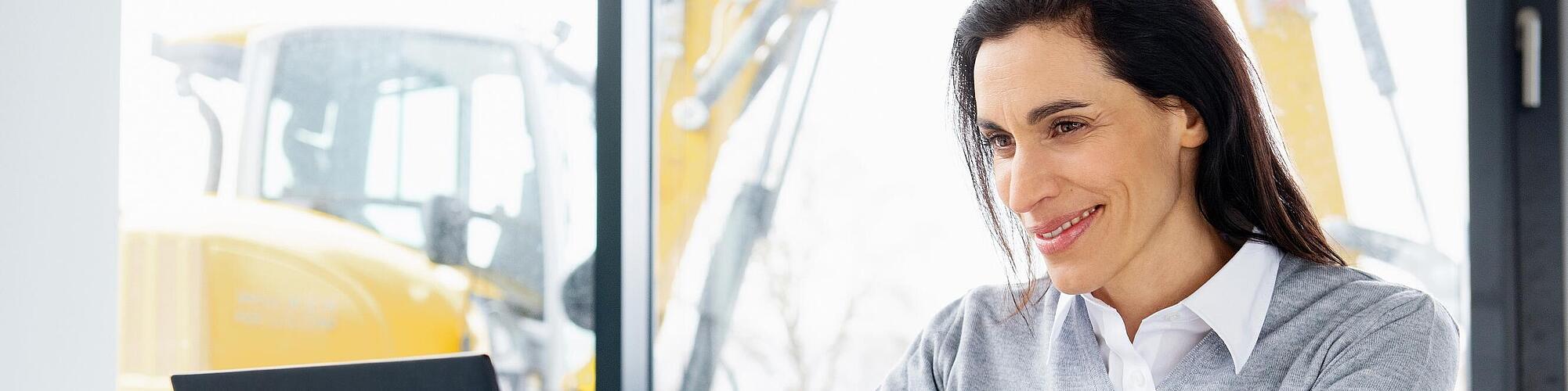 Una empleada de Wacker Neuson está sentada sonriendo frente a un ordenador portátil.