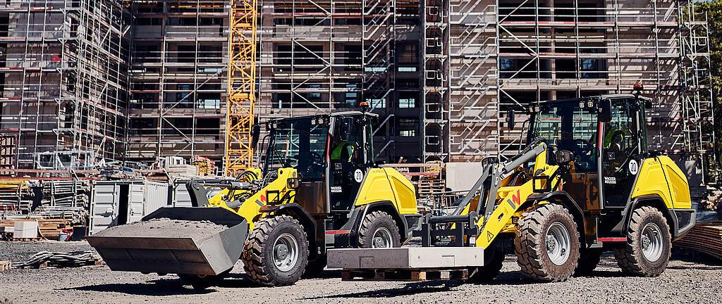 Wacker Neuson WL750p and WL950p wheel loaders on a construction site with a tower crane and building under construction in the background.