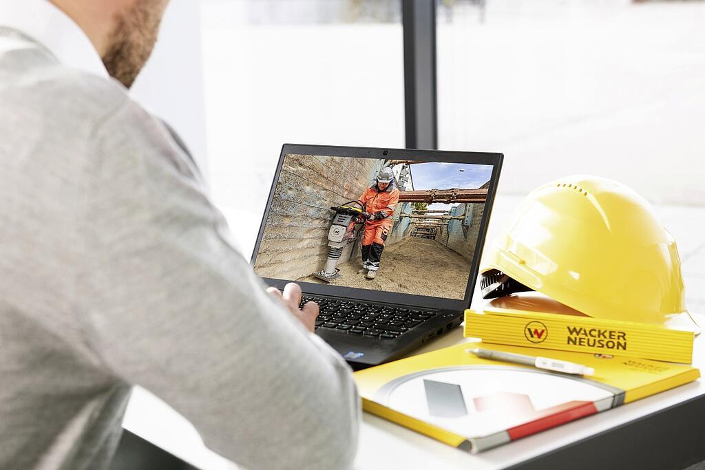 Man at a desk, in front of him is a laptop with the Wackerneuson page open