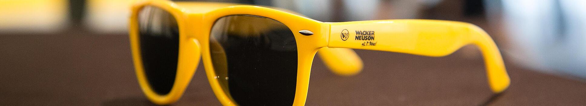 Yellow sunglasses with Wacker Neuson logo.