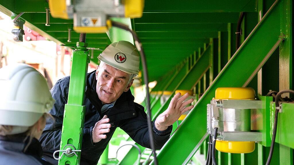 Сотрудник компании Wacker Neuson стоит перед внешним вибратором и рассказывает о нем.