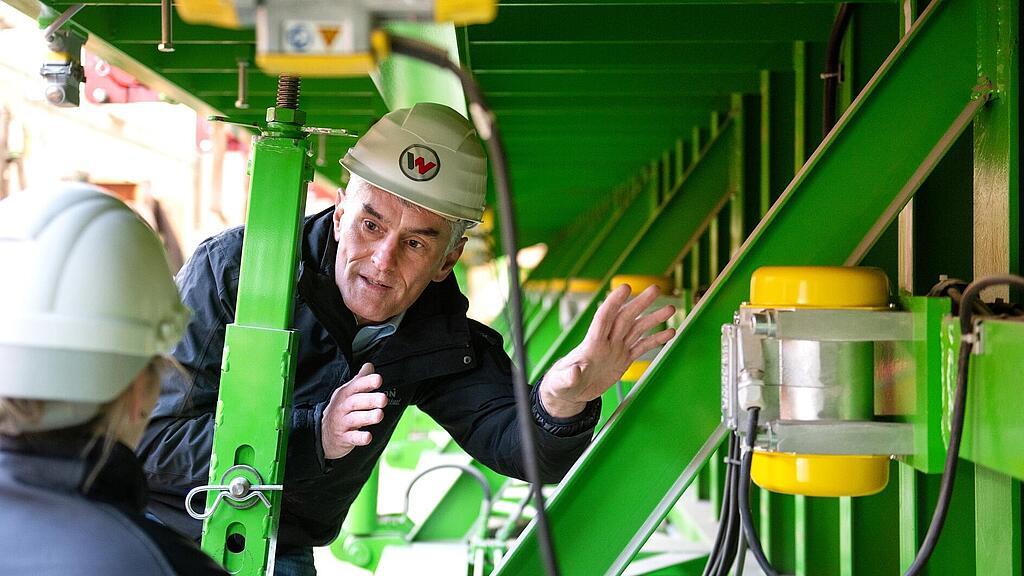 Сотрудник компании Wacker Neuson стоит перед внешним вибратором и рассказывает о нем.