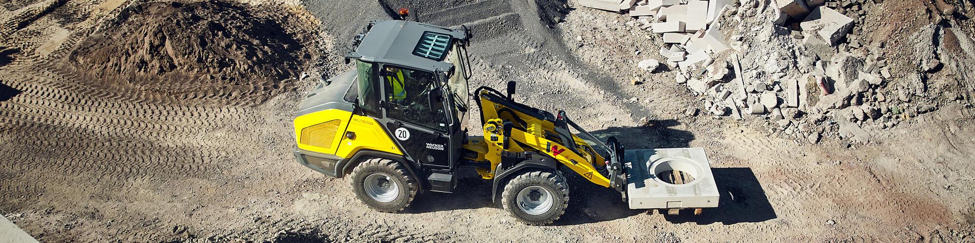 Wacker Neuson WL750p model performanslı tekerlekli yükleyici, bir şantiyede beton elemanı taşıyor.
