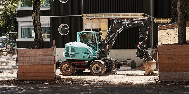 en gravemaskine, der står foran et hus på en byggeplads