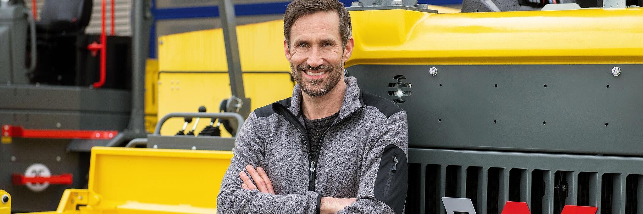 Smiling Wacker Neuson employee, arms crossed, leaning against a Wacker Neuson construction machine.