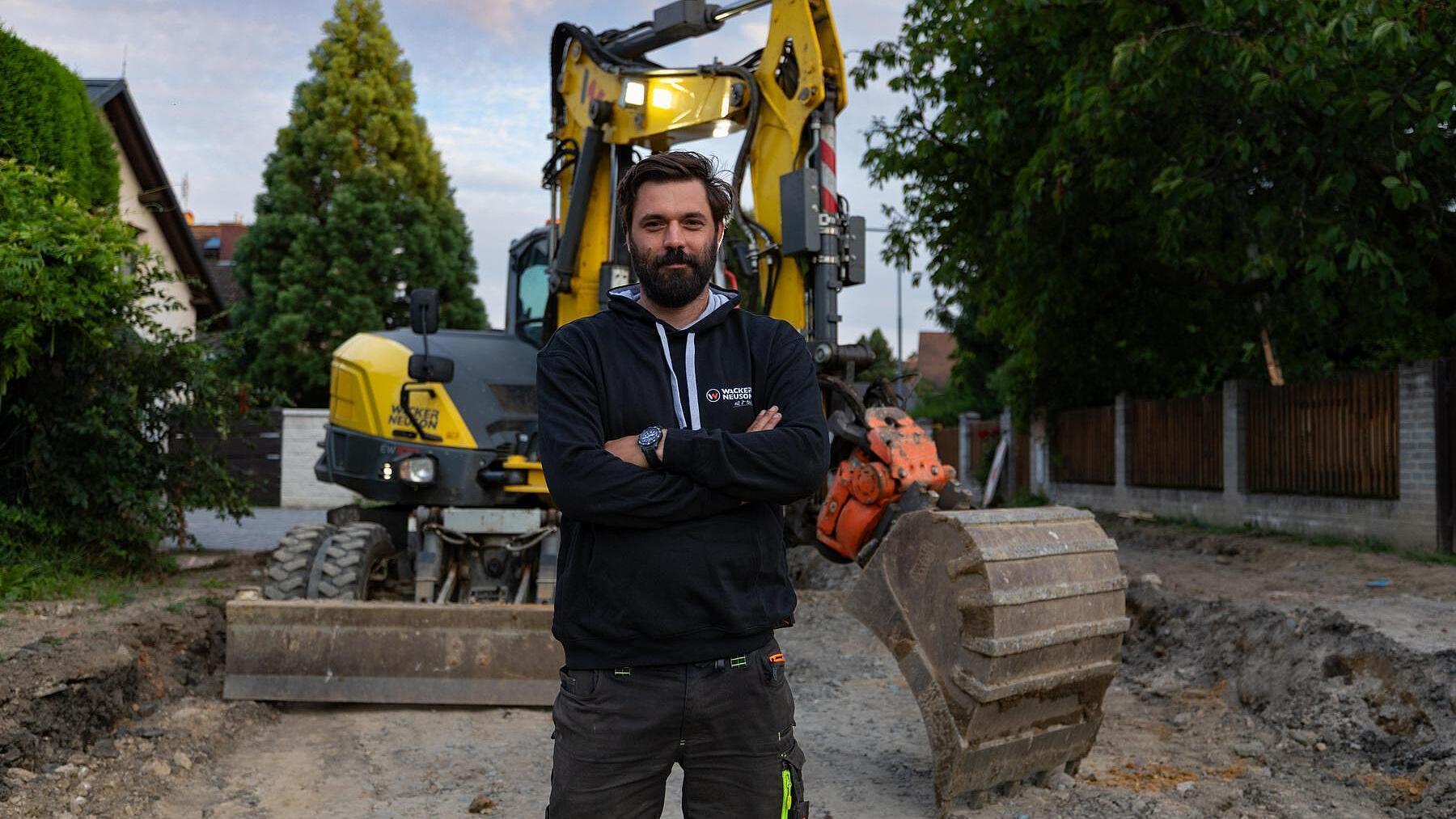 Construction professional standing on a jobsite in front of a Wacker Neuson EW100 wheeled excavator.