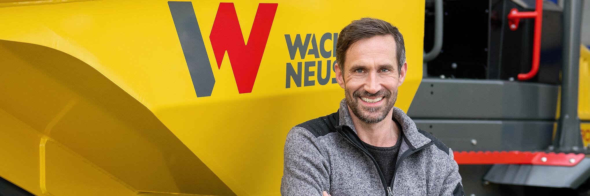 Wacker Neuson customer standing and smiling with arms folded in front of a Wacker Neuson wheel dumper.
