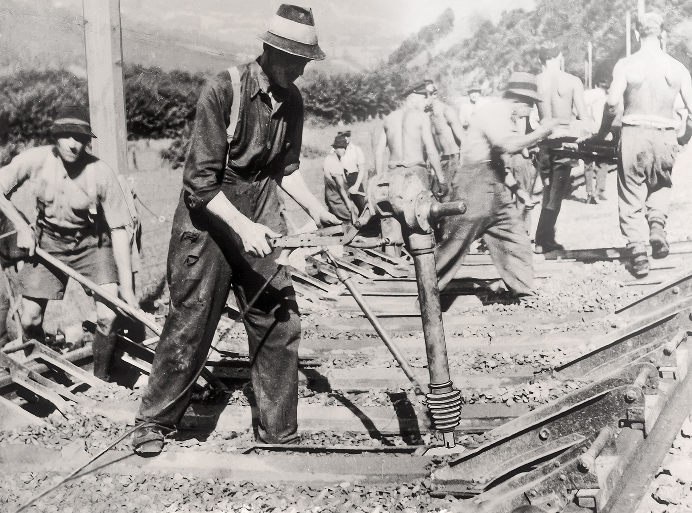 Historic railway workers using manual rammer for track soil compaction on construction site